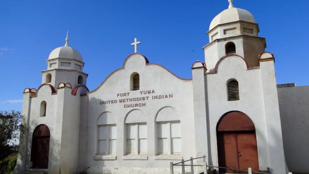 A white mission-style church with two domed towers and arched red doors in Winterhaven