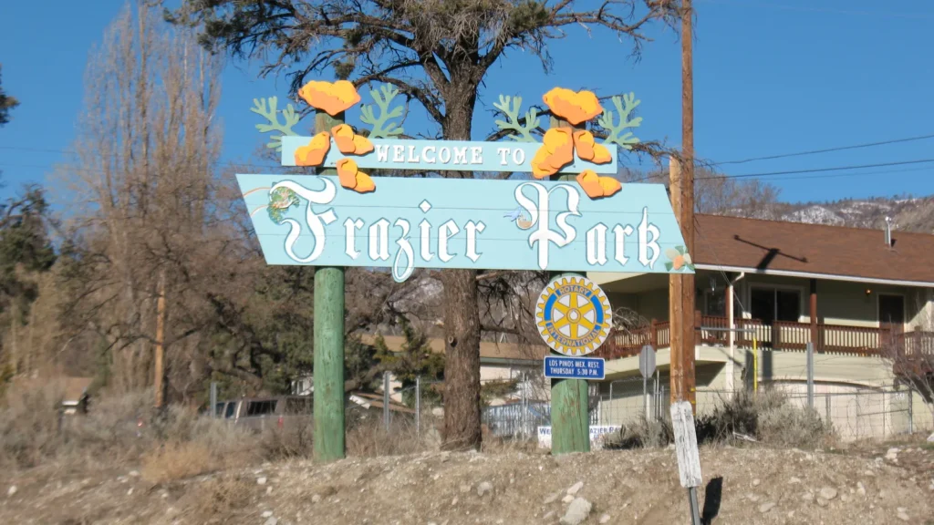 The blue Frazier Park community sign with orange poppies, among pine trees