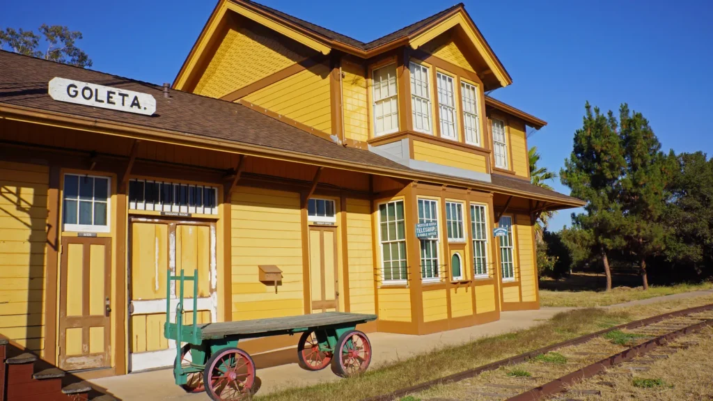 The yellow Victorian Goleta railroad depot with a GOLETA sign and a baggage cart