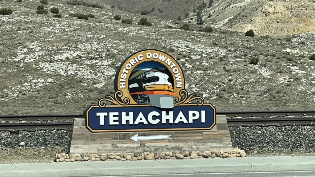 The Historic Downtown Tehachapi sign by the railroad tracks, with hills behind