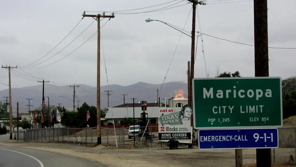 The green Maricopa city limit sign beside a road, with hills behind